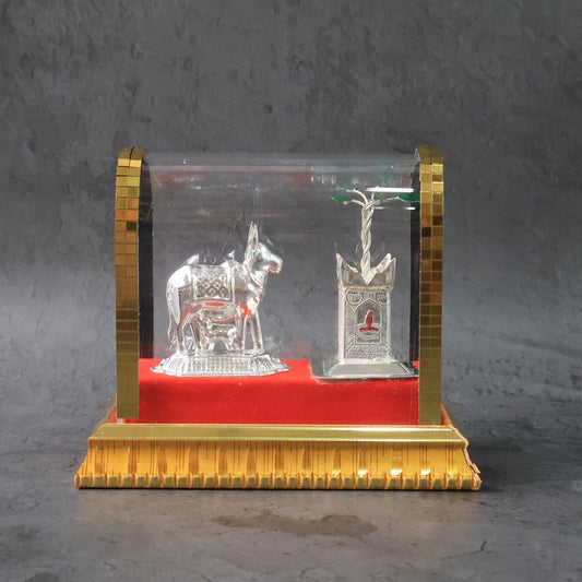 Silver-plated Kamdhenu cow idol set displayed in acrylic case with Tulsi plant